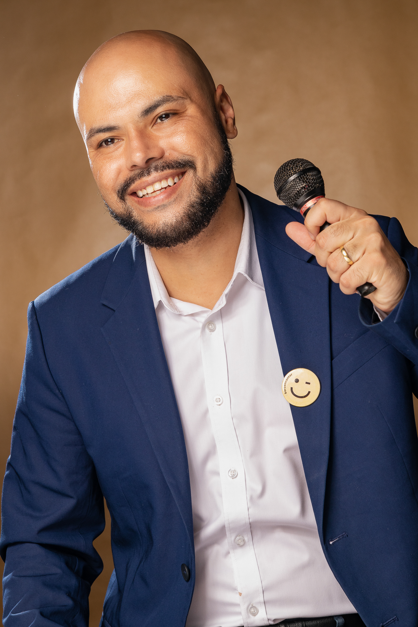 Robson Costa de blazer azul, sorrindo com um microfone na mão